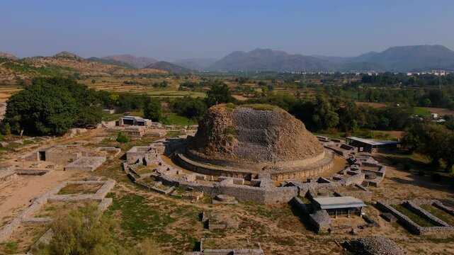 Aerial view of Dharmarajika Stupa ruins amidst scenic fields and trees, Taxila, Pakistan.