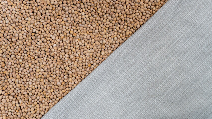 A diagonal layout separates smooth cherry pits and textured fabric. The kernels display earthy tones and rounded shapes. The fabric contrasts with its soft, woven texture and neutral hue