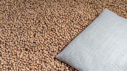 A reusable heating and cooling pillow lies on a layer of cherry kernels. The fabric cover is textured, and the pillow is filled with oval kernels. Designed for use in microwaves and freezers