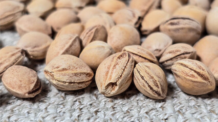 Macro shot of cherry kernels scattered on textured fabric. Oval seeds with visible cracks and grooves. Close-up highlights fine details, earthy tones, and the natural raw texture of the kernels
