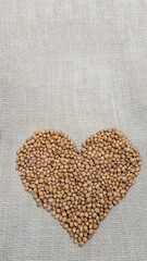 A heart-shaped arrangement of cherry pits lies on a woven fabric background. The smooth, oval seeds in earthy tones create a natural, rustic design. The fabric adds contrast with its neutral texture