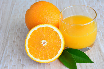 a glass of orange juice with some oranges and green leaves close up