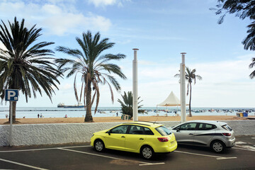 Cars on the beach under palms and blue sky. Parking space for the disabled, for people with disabilities. Santa Cruz de Tenerife, Spain. Playa De Las Teresitas, Atlantic Ocean coast, Canary Islands