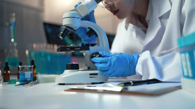 Scientist wearing lab coat and gloves carefully adjusting microscope in laboratory setting
