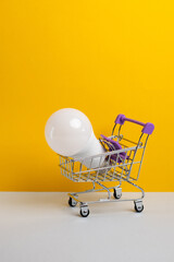 Shopping goods. Shopping cart with light bulbs on yellow background.