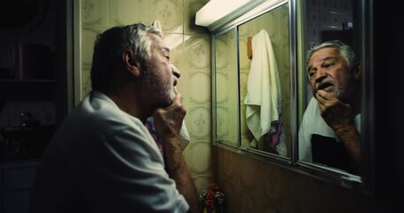 Elderly man leaning into his reflection in a bathroom mirror, eyes filled with intensity, as if searching for lost time and grappling with his own existence