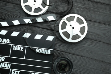 Movie clapper, film reels and camera lens on black wooden table, flat lay