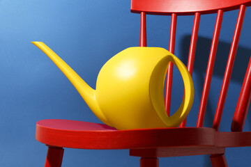 Yellow plastic watering can on chair against blue background