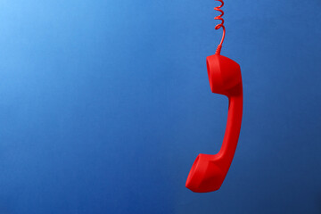 Red corded telephone handset on blue background. Space for text
