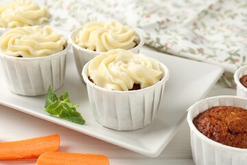 Delicious carrot muffins and fresh vegetable on white wooden table, closeup