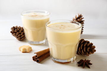 Tasty Christmas cocktail (eggnog) in glasses, pine cones and spices on white wooden table, closeup