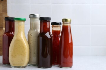 Tasty sauces in glass bottles on white table, closeup. Space for text