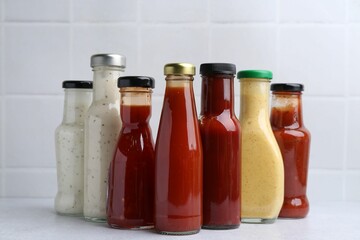 Tasty sauces in glass bottles on white table, closeup