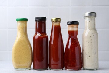 Tasty sauces in glass bottles on white table, closeup