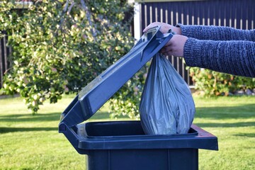 Woman throws plastic bag of garbage into green street trash bin.
