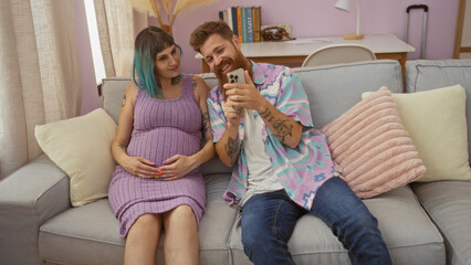 Pregnant woman and man sitting on sofa together in colorful living room, looking at a phone and smiling, with pastel decor and natural light filling the cozy home interior.