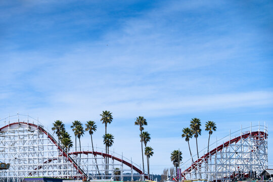View of santa cruz beach boardwalk with roller coaster and palm trees under a blue sky, santa cruz, california, usa.