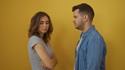Man and woman standing over yellow background, appearing to be in a tense discussion or conflict,...