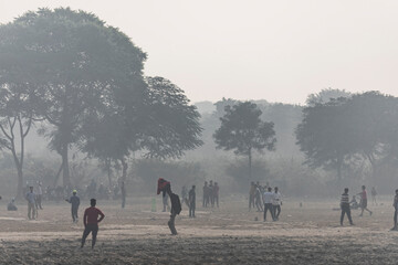 Agra, India - 01 December 2024: View of people playing cricket in a foggy park surrounded by trees, Agra, India.