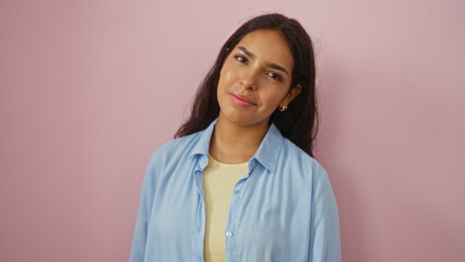 Fototapeta premium Young woman with brunette hair wearing a blue shirt stands over an isolated pink background, showcasing a beautiful and confident expression