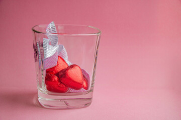 Heart-shaped candies and silver ribbon in a glass on a pink background