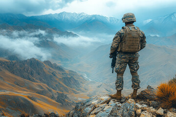 Fototapeta premium Amidst misty mountains, a soldier in camouflage stands firm upon a rugged rock, gripping his weapon with a determined gaze
