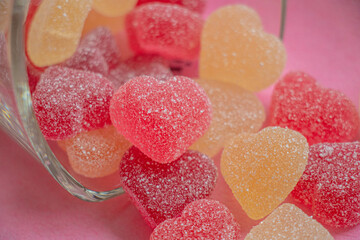 Multicolored Valentine's Day gummy hearts spilling out of glass on pink background, close up