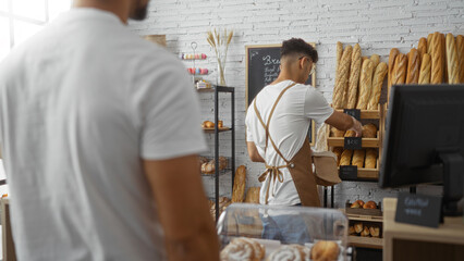 Hispanic men in a bakery setting with one as a worker arranging bread and the other as a customer,...