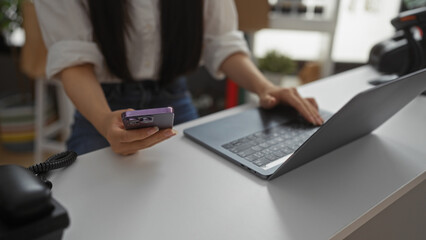 Fototapeta premium Young woman in a decoration store using a phone and laptop, focusing on her hands interacting with technology in an indoor, home decor setting.