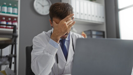 Frustrated doctor man in clinic office wearing white coat stressed at work shown with hand on...