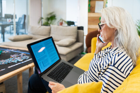 Senior Woman Reviewing Document on Laptop While on Phone