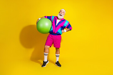Obraz premium Full length photo of attractive funny retired sportsman retro sportswear holding fitball emtpy space isolated yellow color background
