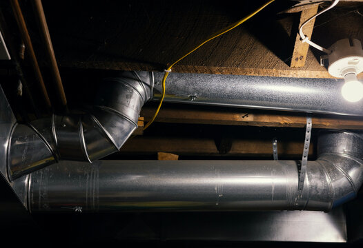 Single light bulb illuminates metal duct work in old dusty basement