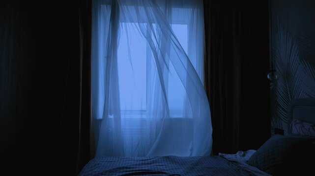 without people, empty dark room modern bedroom, white chiffon tulle fly, silk curtain fluttering waving from wind blow ventilation draft. Night twilight early morning dusk blue light. double bed made