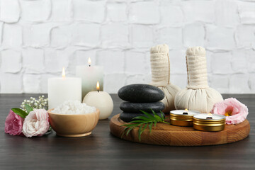 Massage bags, spa stones, sea salt, burning candles and flowers on wooden table