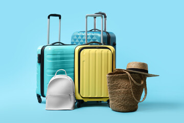 Colorful suitcases, backpack, beach bag and straw hat on light blue background