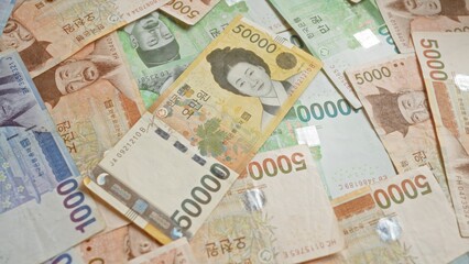 South korean banknotes scattered on a surface, showcasing various denominations and intricate designs of won currency.