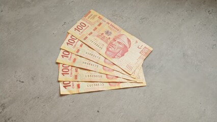 Mexican banknotes worth 100 pesos each are fanned out on a concrete surface, showcasing the...