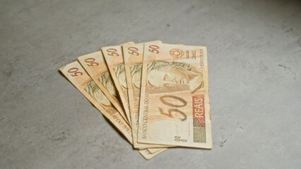 Brazilian banknotes of 50 reais neatly spread on a concrete surface, showcasing the central...
