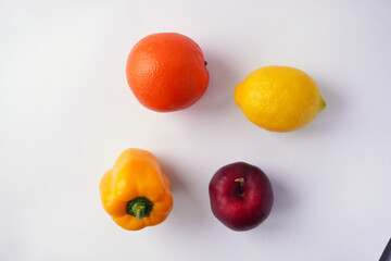 A vibrant arrangement of an orange, a lemon, a yellow bell pepper, and a red apple placed on a clean white background, highlighting their natural colors and textures in a minimalistic style.
