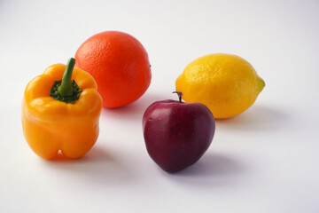A vibrant arrangement of a red apple, lemon, orange, and yellow bell pepper on a white background showcasing fresh produce.