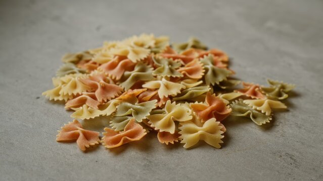 Colorful farfalle pasta scattered on grey concrete surface creating a vibrant and appetizing scene with uncooked italian food elements centered