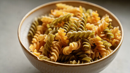 Closeup shot of multicolored fusilli pasta in a ceramic bowl placed on a textured gray surface, highlighting the detail and vibrancy of the uncooked spiral noodles.