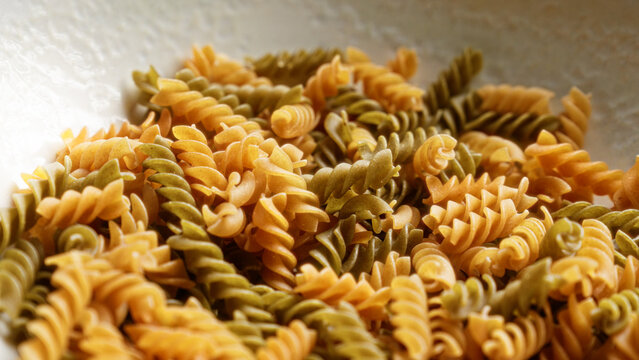 Close view of tricolor fusilli pasta against a neutral background depicting uncooked curly pasta