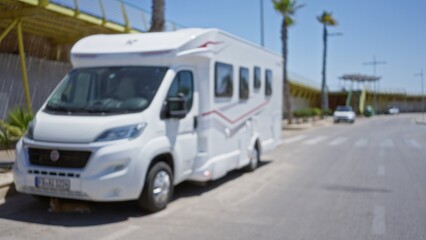 Defocused camper parked outdoors on a sunny day with palm trees and blue sky in the background