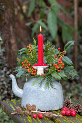 Silvester-Arrangement mit roter Kerze, Stechpalmenzweigen und Koniferenzweigen im alten Teekessel	