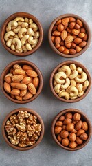 Healthy assortment of raw nuts in small terracotta bowls on grey concrete background - cashews, almonds and walnuts rich in protein and healthy fats for snacking or cooking.