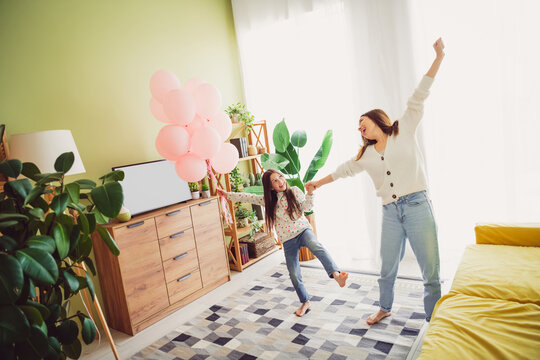Joyful young mother and daughter dancing playfully at home on a sunny spring day