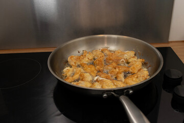 Metal frying pan on glass stove. Chicken pieces are fried in the pan. Home cooking