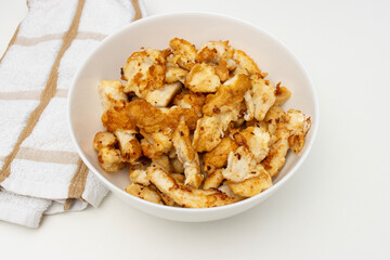 fried chicken pieces in white bowl. Dinner on white table. Close-up, copy space, top view